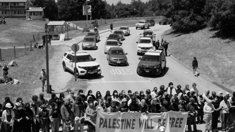 foto of protestors blocking the base of campus at UCSC. A large banner reads "Palestine will be free".